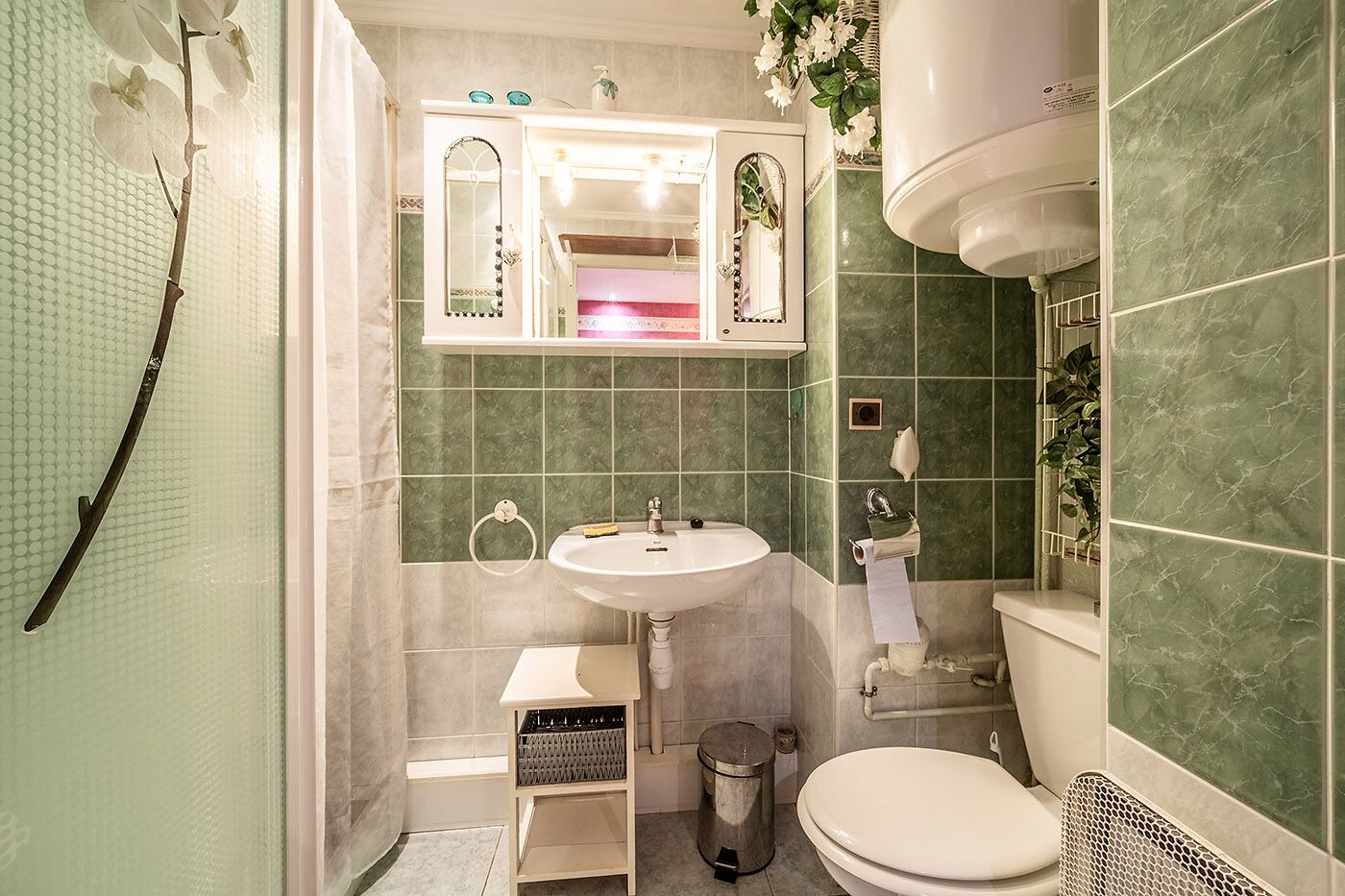 A bathroom with a white sink, green tiled walls, a toilet, and a shower area.