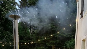Un jacuzzi con revestimiento de madera y un calentador metálico, rodeado de un jardín con luces colgantes y árboles.