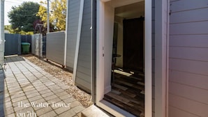 Ein Wohnhaus mit gepflasterter Terrasse, einer Tür zu einem Raum und einem eingezäunten Garten.