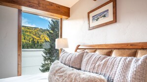 Une chambre avec une grande fenêtre, une tête de lit en bois et un tableau encadré accroché au mur.