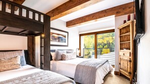 Une chambre avec deux lits, des poutres en bois, une fenêtre donnant sur les arbres et une armoire en bois.