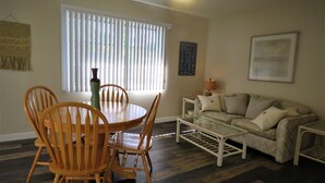 A dining area with a round wooden table and chairs, a glass coffee table, and a sofa with cushions. - 2 bed/2 Ba Venice Island Villa - Walk to Beach & Historic Downtown Venice! (Venice)
