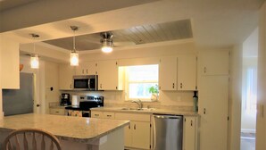A modern kitchen with white cabinets, a central island, stainless steel appliances, and a window providing natural light. - 2 bed/2 Ba Venice Island Villa - Walk to Beach & Historic Downtown Venice! (Venice)