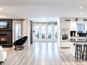 A modern kitchen with white cabinetry, a central island with stools, a microwave, and a stove.