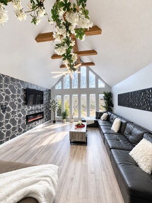 A modern living room with a stone wall, a fireplace, a leather sofa, and a large window.