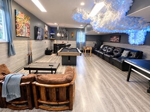 A modern living room with a pool table, a foosball table, a sofa, and a ping pong table.