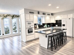 A modern kitchen with a central island, bar stools, and a view of snow-covered trees.