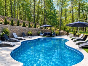 A swimming pool with lounge chairs and umbrellas, surrounded by a landscaped garden and trees.
