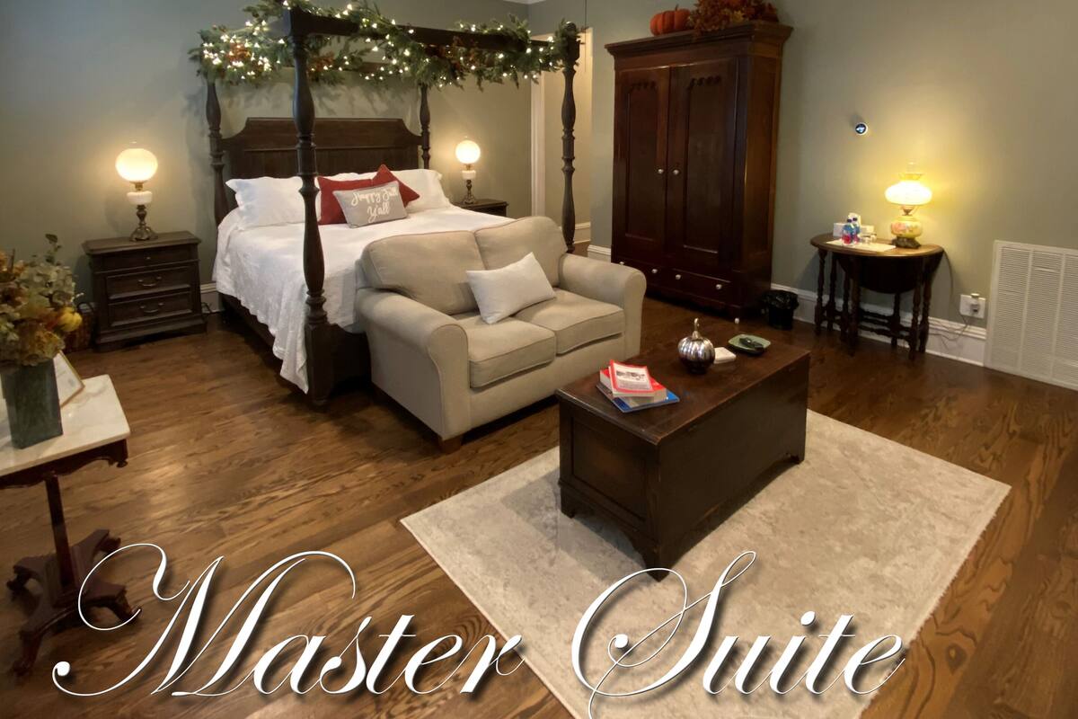 Een masterslaapkamer met een hemelbed, een zithoek met een bijzettafeltje en een ruime garderobe.