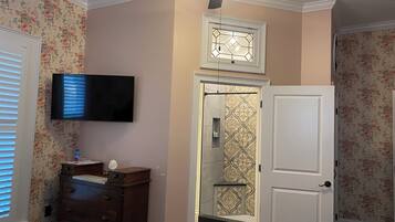 Ein Schlafzimmer mit Bett, Schminktisch, Fernseher, Deckenventilator und einer Badezimmertür.