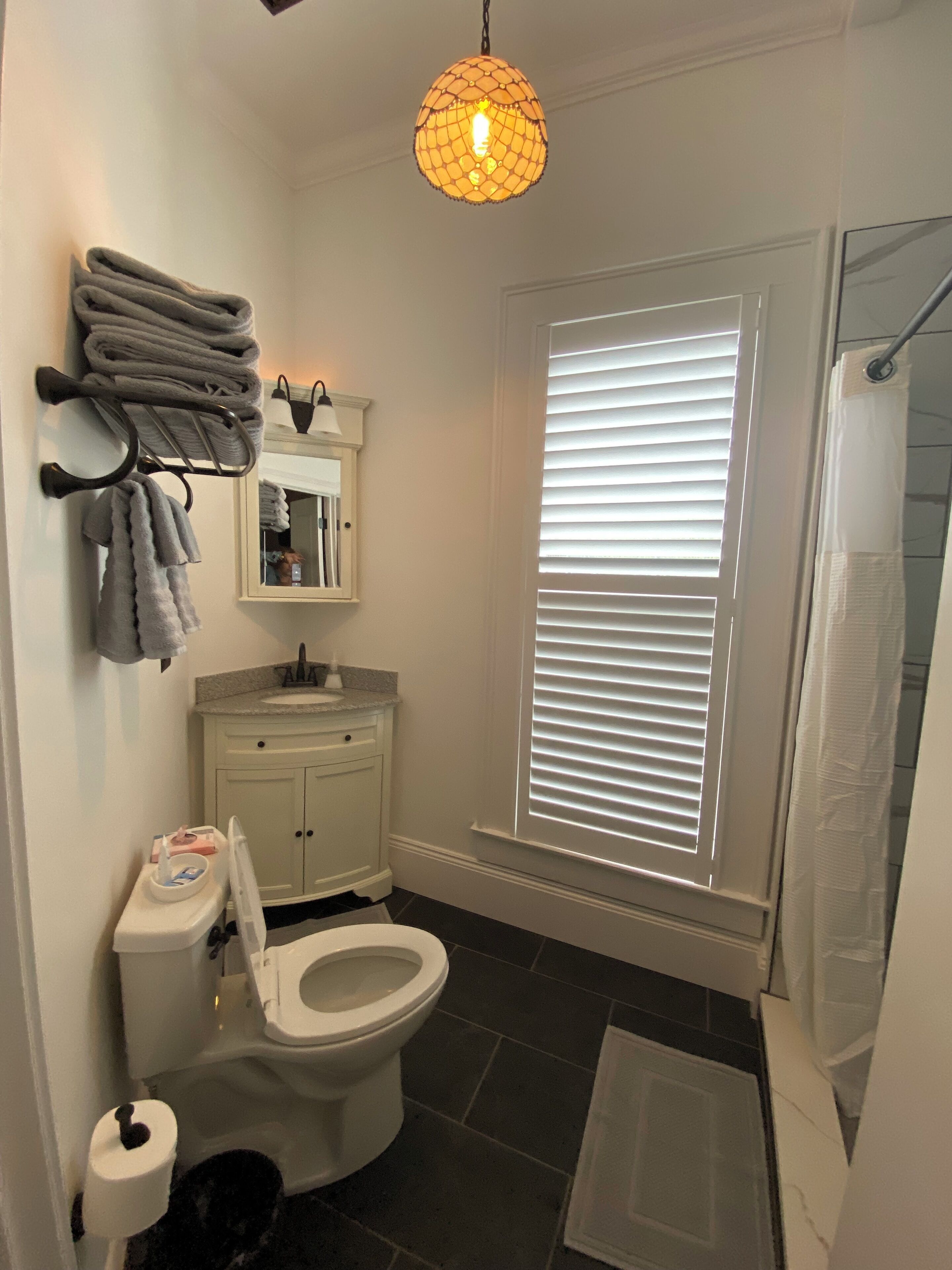 A bathroom with a toilet, sink, towel rack, and a window with blinds.