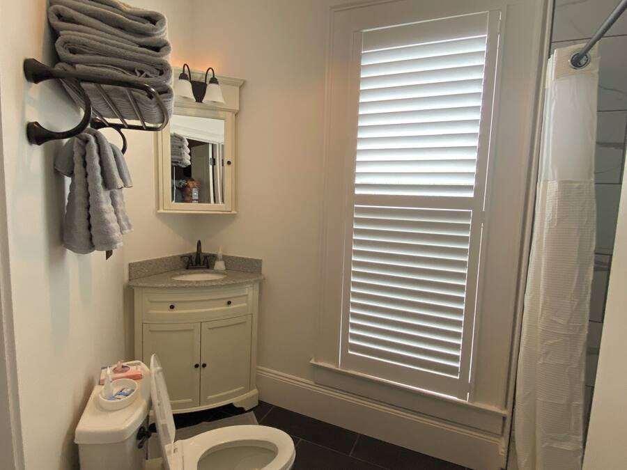 A bathroom with a toilet, sink, towel rack, and a window with blinds.