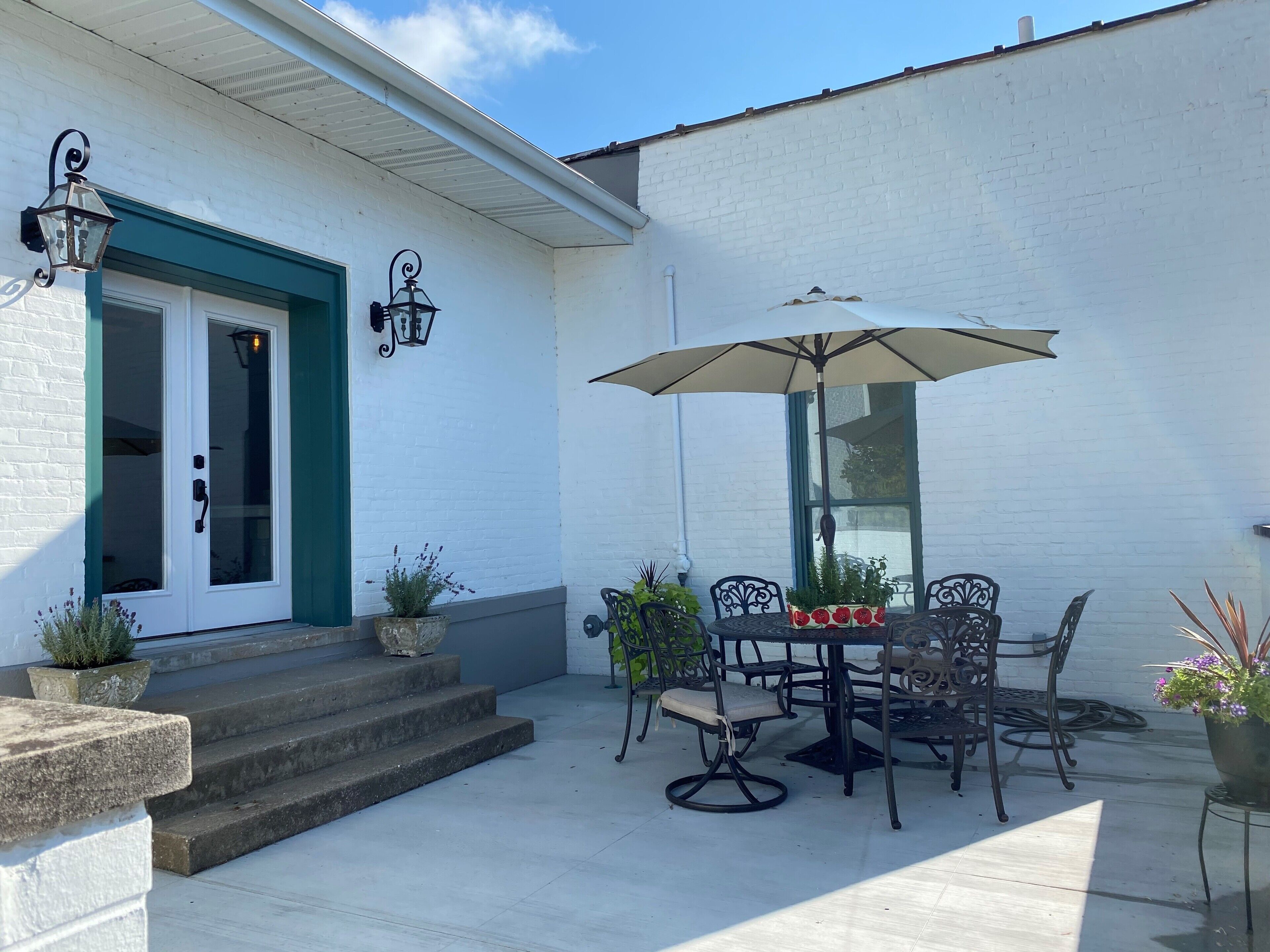 A patio with a table and chairs, an umbrella, and potted plants.