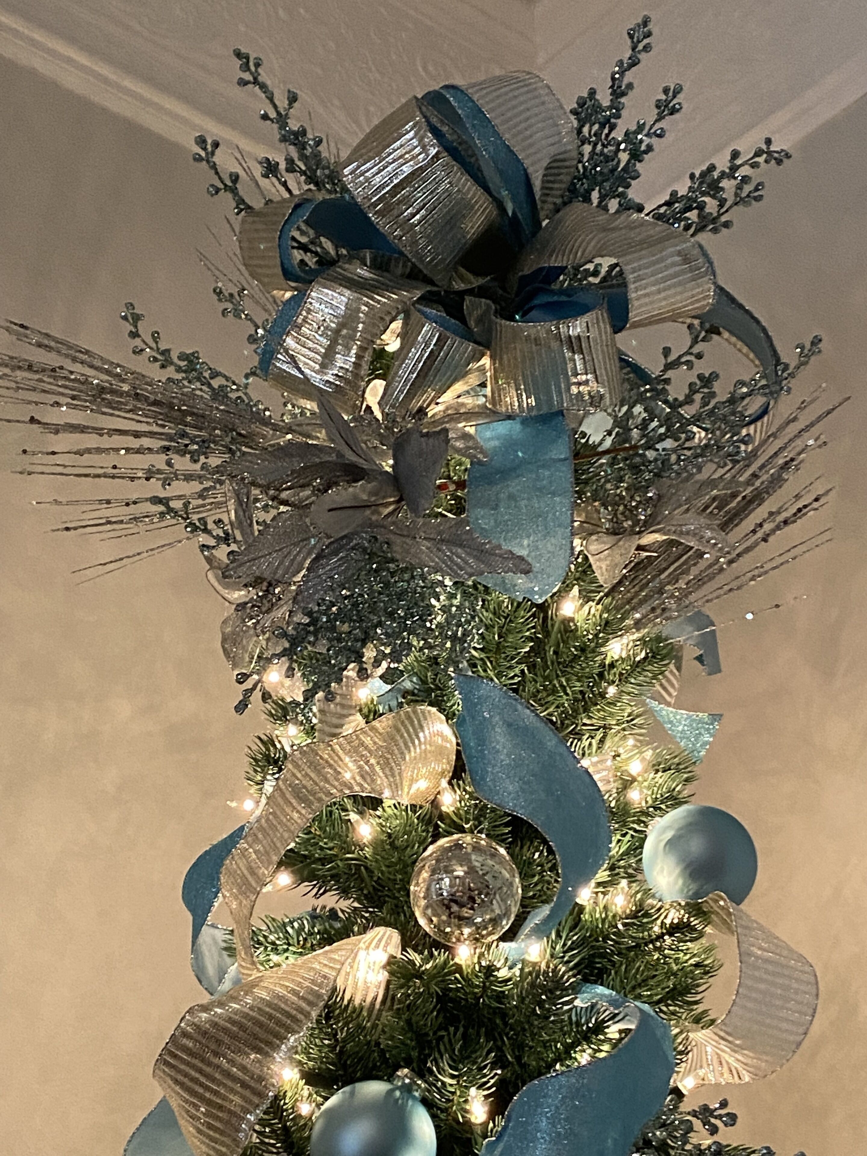 Een kerstboom met een grote blauwe lint strik en zilveren versieringen.