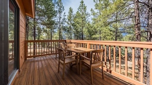 A wooden deck with a table and chairs, overlooking a forested area. - Flagstaff | Mountain Retreat | Pool & Golf | 2BR Condo (Flagstaff)