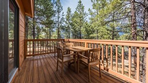 A wooden deck with a table and chairs, overlooking a forested area.