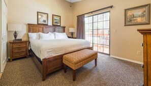A bedroom with a large bed, two bedside tables, a bench, a window with curtains, and a door.
