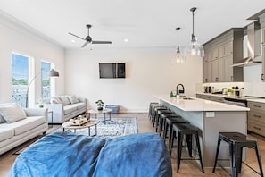 A modern kitchen with a central island, bar stools, and a dining area with a sofa and coffee table.