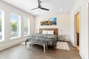 A modern bedroom with a large bed, a ceiling fan, and a cityscape painting on the wall.