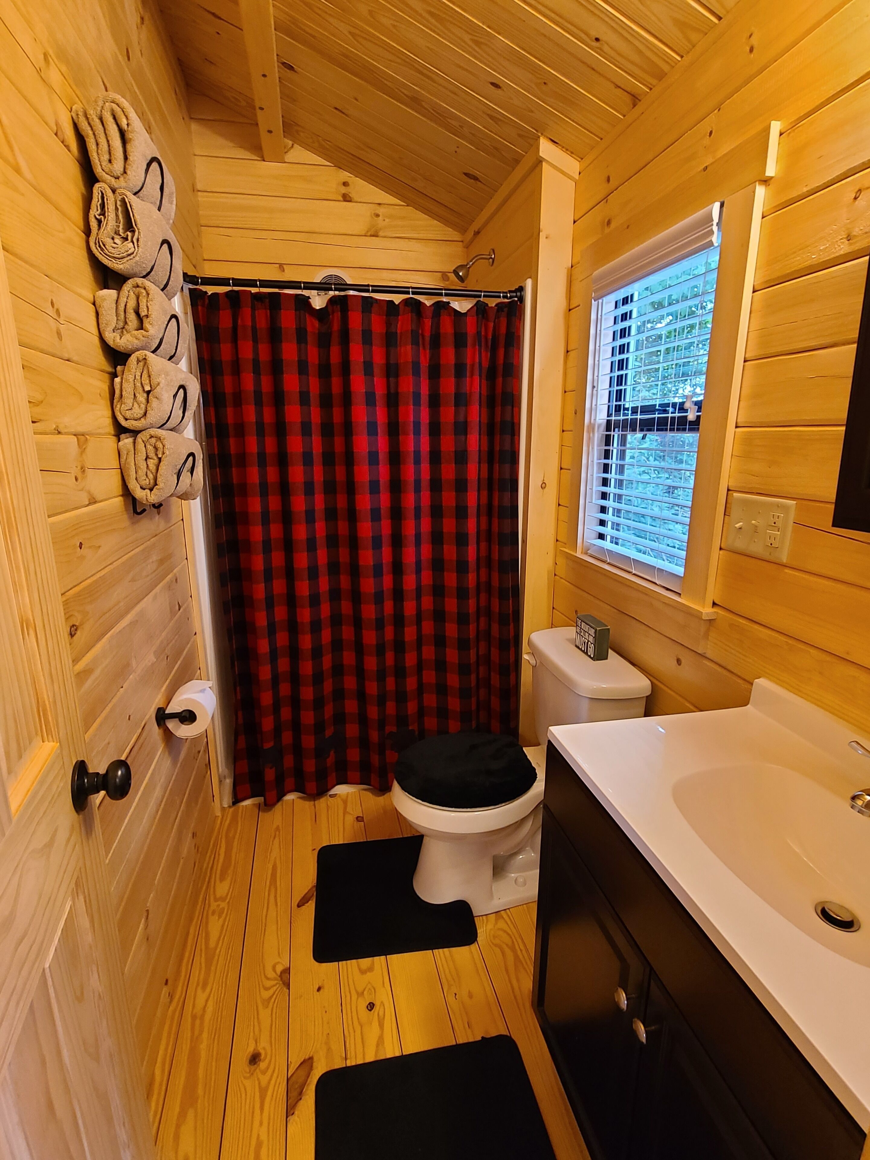 Une salle de bain rustique, aménagée dans une cabane en bois, avec des toilettes, un lavabo et un rideau de douche.