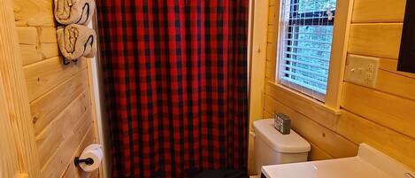 Une salle de bain rustique, aménagée dans une cabane en bois, avec des toilettes, un lavabo et un rideau de douche.