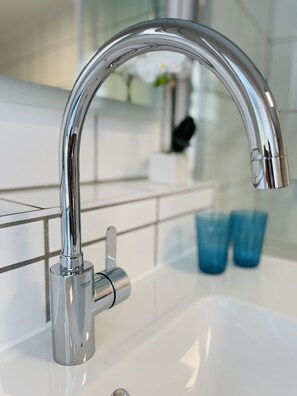 Ein modernes Badezimmer mit einem chromfarbenen Wasserhahn, einem weißen Waschbecken und einer Glasabtrennung.