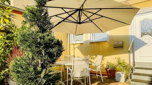 A patio area with a table and chairs, a large potted plant, and a white umbrella. - Historic vacation home on the Main, 110 sqm, large terrace, modern and renovated (Mainz-Kostheim)