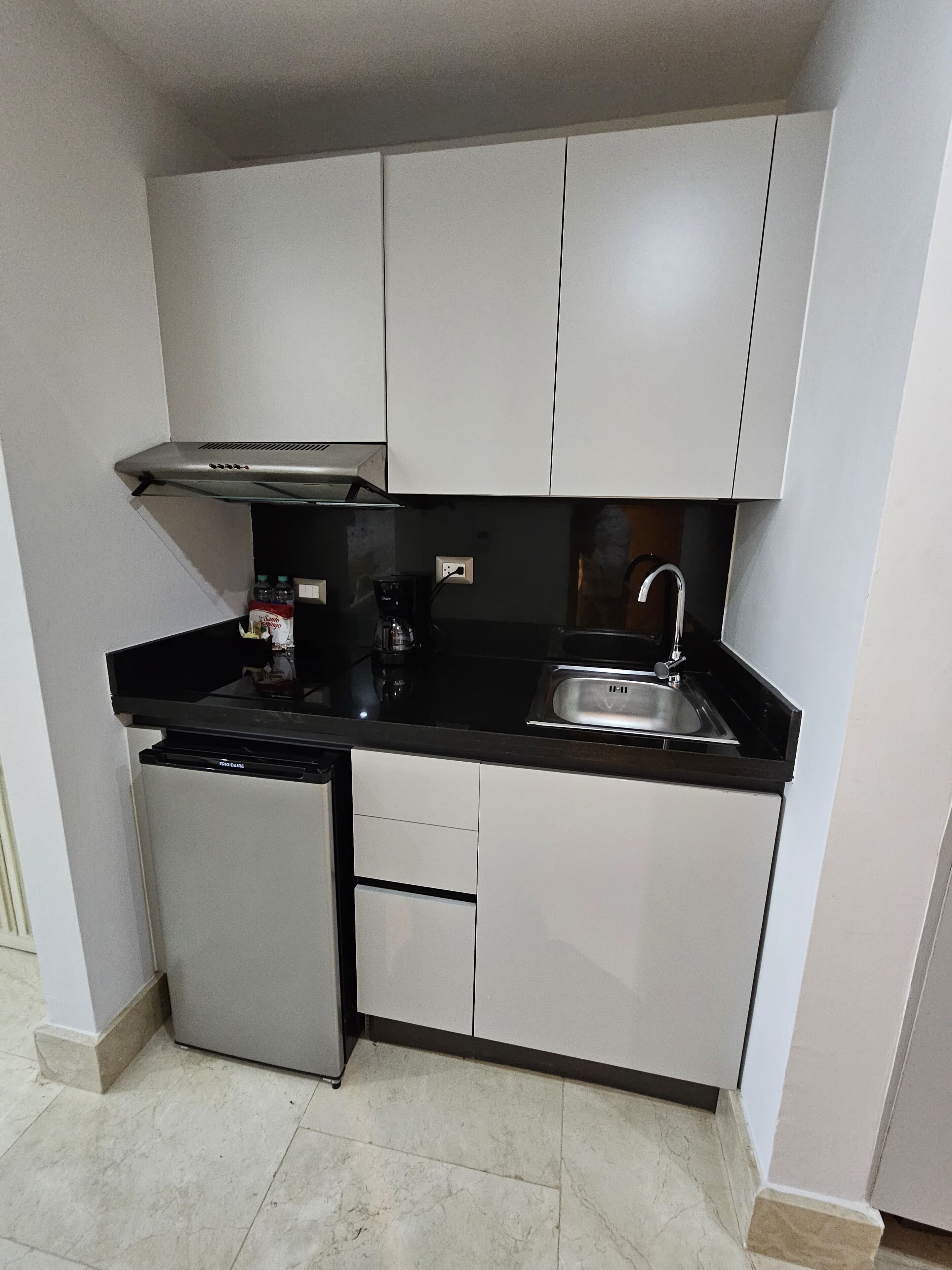 A compact kitchen with a refrigerator, a coffee maker, and a sink.