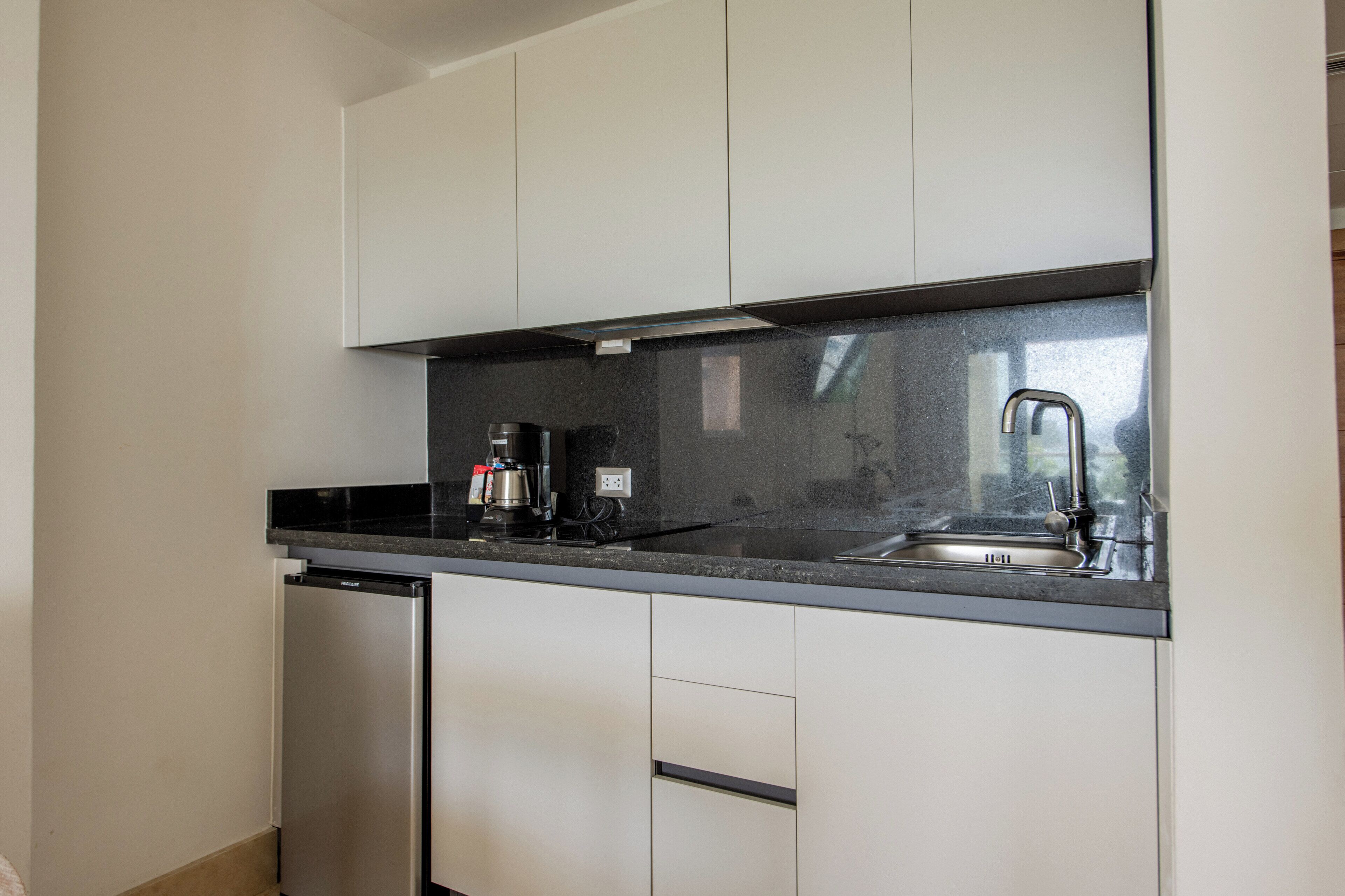 Una cocina compacta con armarios blancos, lavavajillas de acero inoxidable, cafetera y pileta.