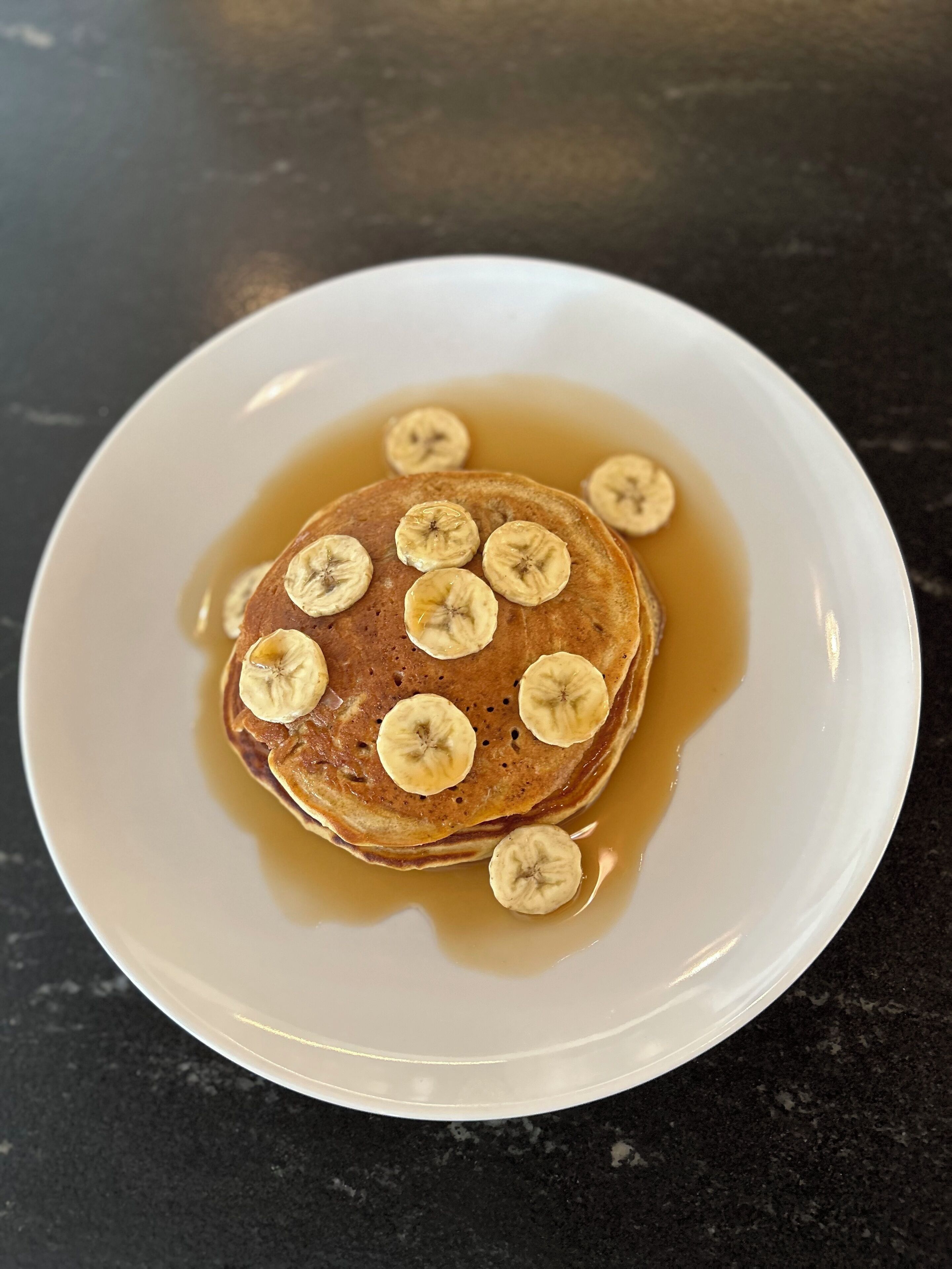 A plate with pancakes topped with banana slices and syrup.