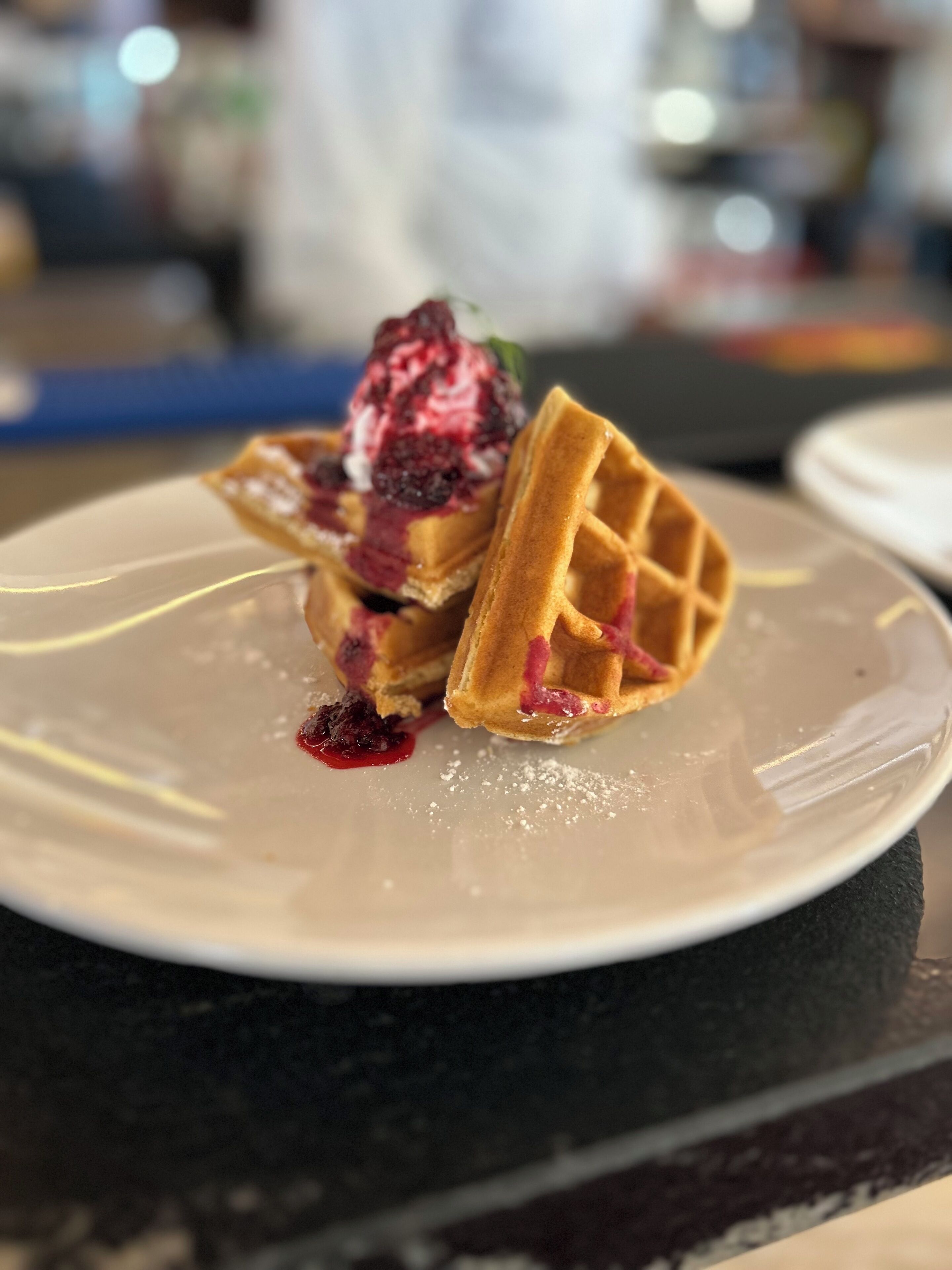 A close-up of a dessert with a waffle, berry compote, and a scoop of ice cream on a white plate.