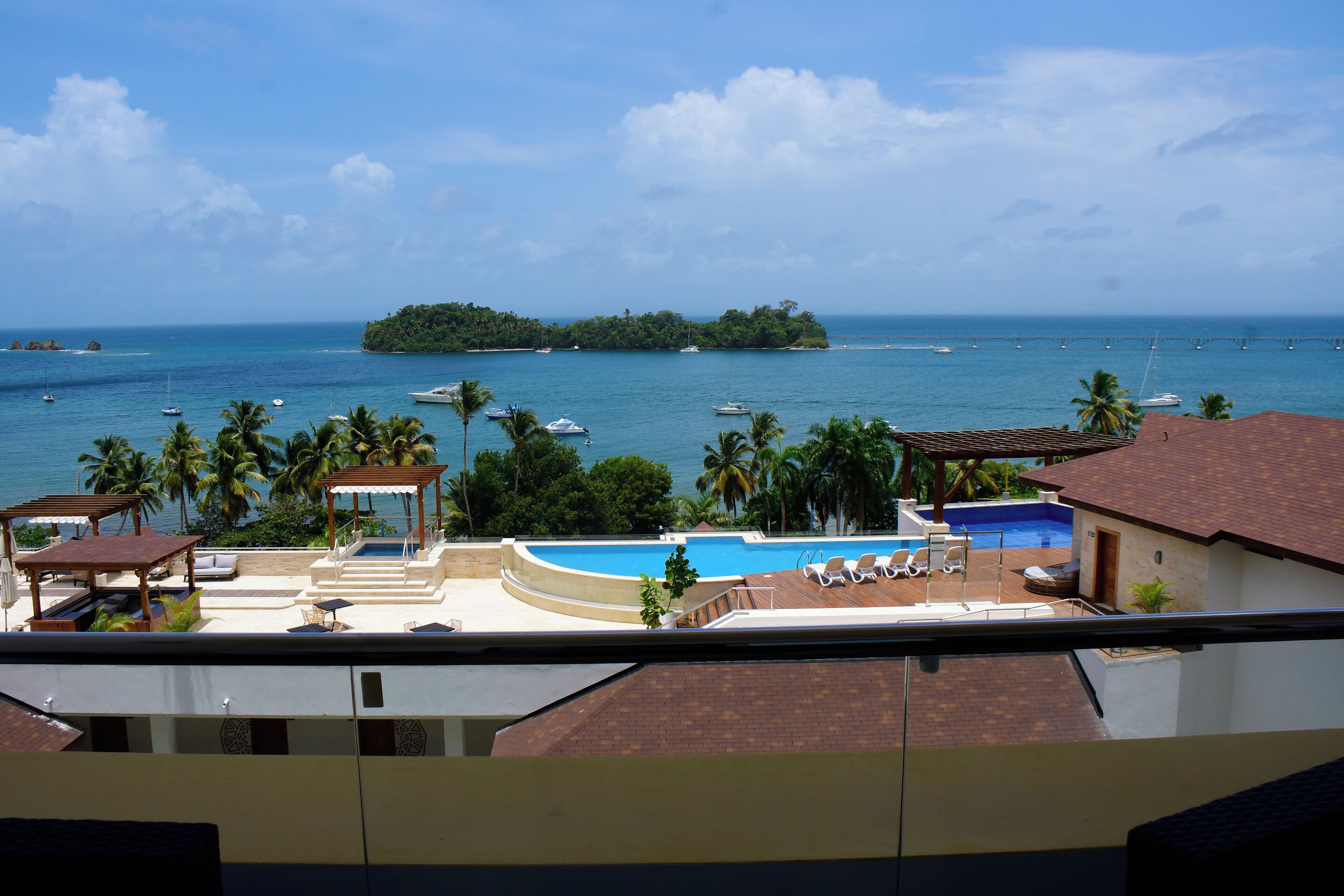 A resort with a swimming pool, lounge chairs, and a view of the ocean and a small island.