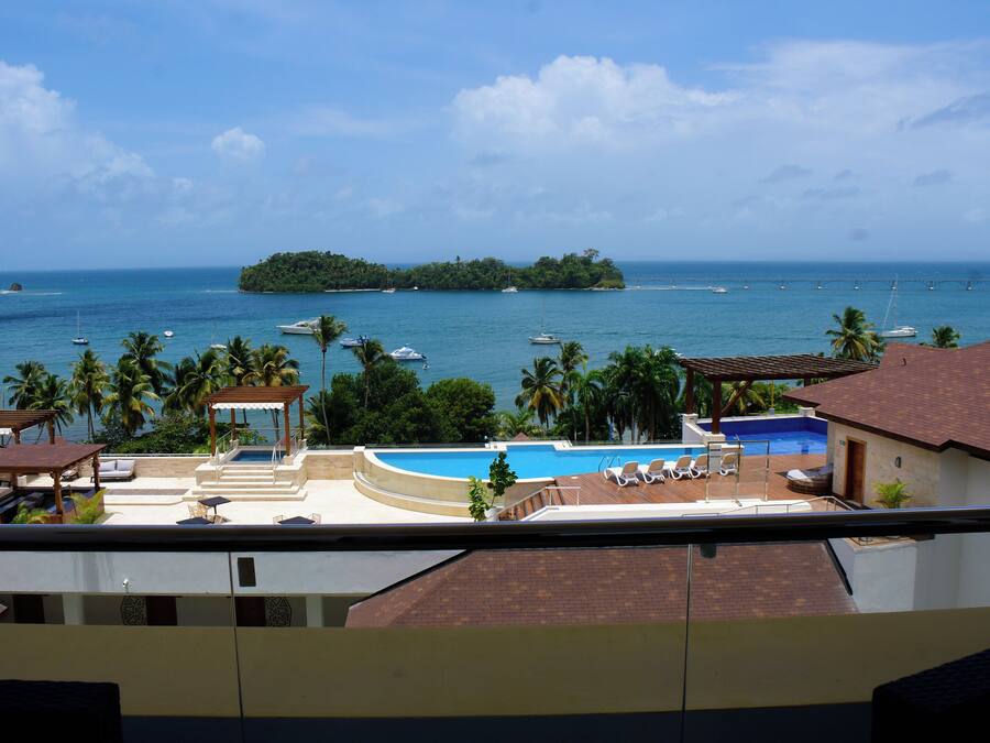 A resort with a swimming pool, lounge chairs, and a view of the ocean and a small island.