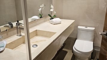 Ein modernes Badezimmer mit einem großen Waschbecken, zwei Wasserhähnen, einer Toilette und einer kleinen Mülltonne.