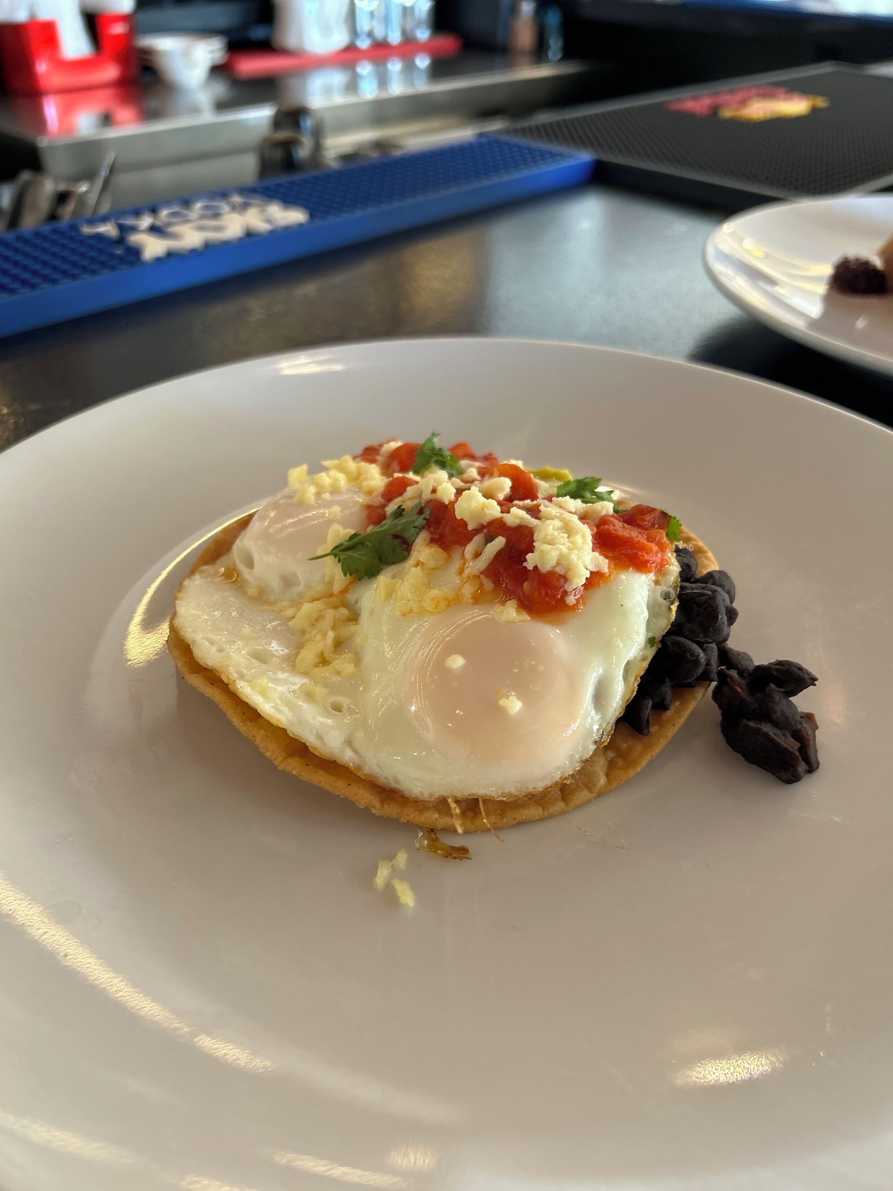 Un plato con un huevo frito, queso, tomate y frijoles negros sobre un plato blanco.