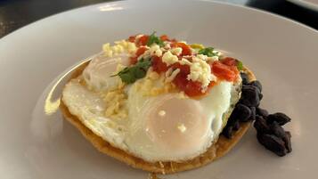 Un plato con un huevo frito, queso, tomate y frijoles negros sobre un plato blanco.