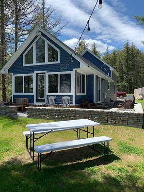 Ein blaues Haus mit einer Steinterrasse, Sitzmöglichkeiten im Freien und einem Picknicktisch.