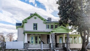 A two-story house with a green porch and stone steps. - The Historic Magnolia House (Greensboro)