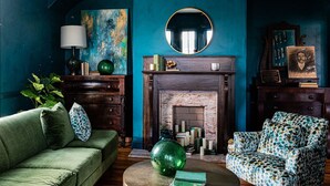 A room with a fireplace, a round mirror, a green sofa, a patterned armchair, and a bookshelf. - The Historic Magnolia House (Greensboro)