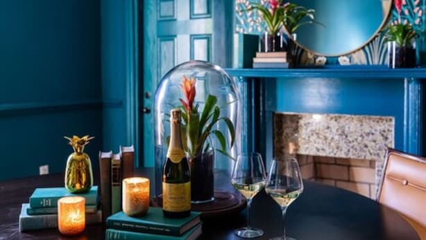 A dining table with a bottle of wine, two glasses, a candle, and a decorative glass dome over a plant. - The Historic Magnolia House (Greensboro)