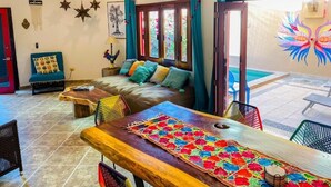 A cozy living room with a sofa, coffee table, and chairs. There is a pool visible through the glass doors. - Casa Boho 1 (Sayulita)
