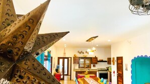 A dining area with a long table and colorful chairs, a kitchen in the background, and a large decorative metal piece in the foreground. - Casa Boho 1 (Sayulita)