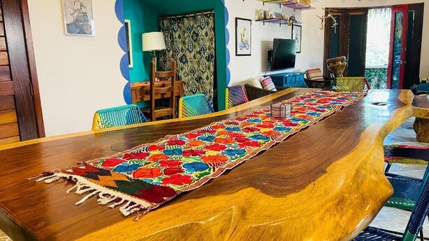 A long wooden dining table with a colorful woven runner, surrounded by colorful chairs. - Casa Boho 1 (Sayulita)