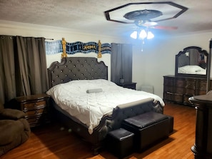 A bedroom with a large bed, a chest of drawers, a dresser, and a ceiling fan.