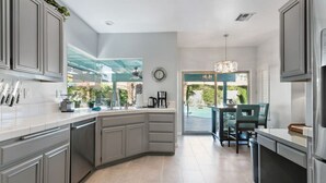 A modern kitchen with grey cabinetry, a central island, and a dining area with a table and chairs.