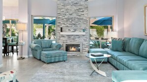 A modern living room with a stone fireplace, comfortable seating, and large windows overlooking a garden.