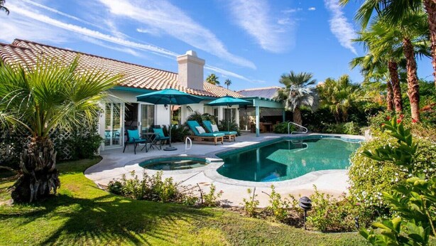 A poolside area with lounge chairs and umbrellas, a swimming pool, and a building with a tiled roof.