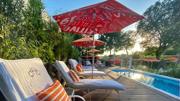 Un espace aménagé au bord de la piscine, avec des chaises longues et des parasols, une piscine, et une enseigne indiquant « HÔTEL ».