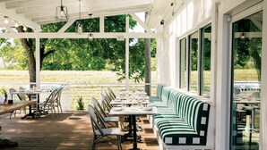Une terrasse extérieure avec un long banc rayé de vert et de blanc, des tables et des chaises.