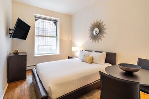 Une chambre à coucher moderne avec un grand lit, une table de chevet, un téléviseur fixé au mur et un miroir décoratif.